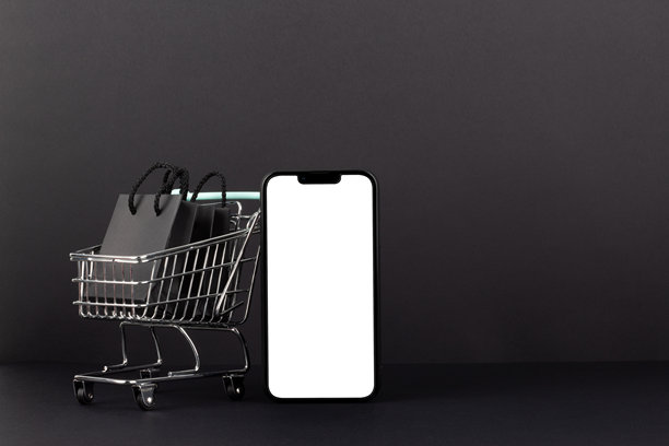 黑色背景下，购物车旁边放着手机模型，购物车内装有购物袋，黑色星期五概念。图片下载