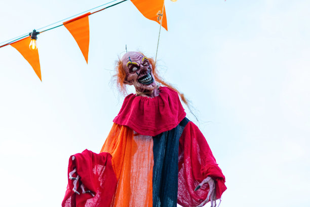 背景是白色天空的悬挂在绳子上的令人毛骨悚然的小丑装饰品图片下载