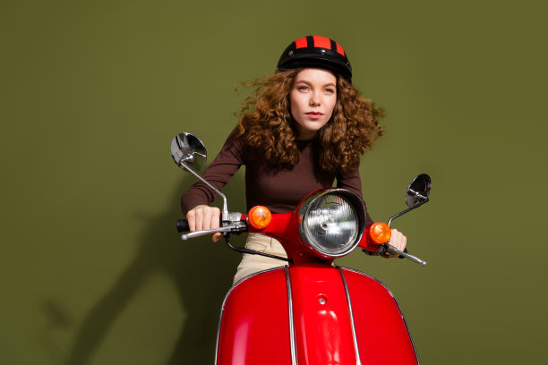 穿着棕色衣服和安全帽的快乐漂亮少女骑着摩托车，背景为空旷的绿色。图片下载