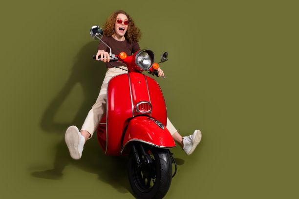 穿着棕色衣服的快乐兴奋的少女全身照，骑着摩托车，背景为空旷的绿色。图片下载