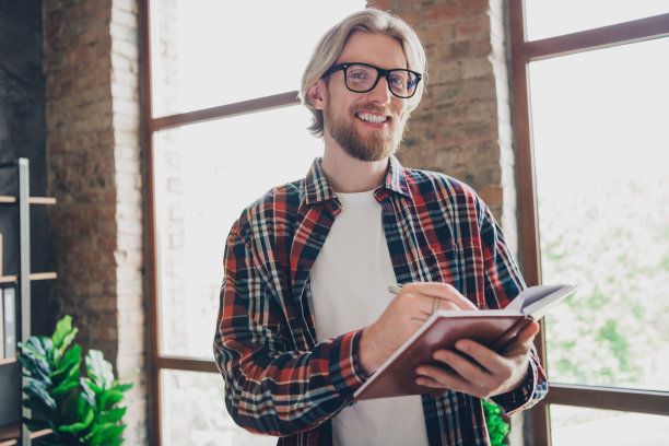 英俊年轻男士的照片肖像，聪明的首席执行官在共享办公空间中写入笔记本，获取更多信息以赚取更多钱。图片下载
