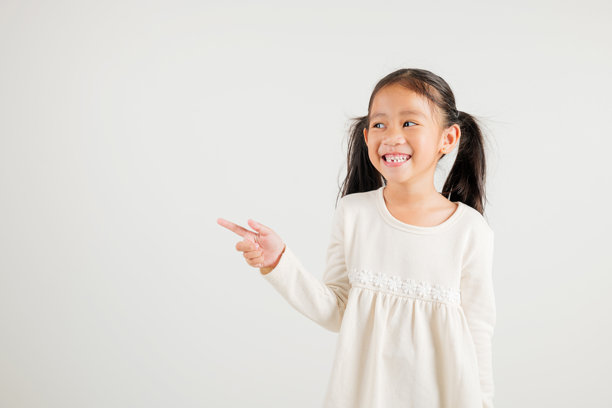 快乐的亚洲小女孩微笑着用手指指向空白处，工作室拍摄，背景为白色。图片下载
