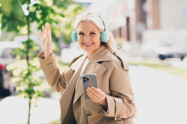 迷人的退休女士在春天散步，心情愉快，戴着耳机听音乐，穿着米色外套，享受周末的户外闲暇时光。图片下载