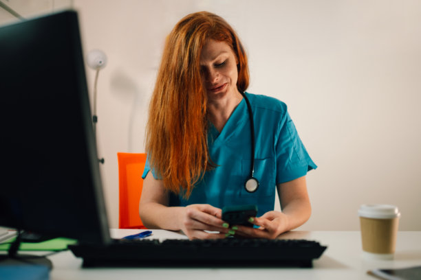 医疗专业人士在桌子上使用智能手机，佩戴听诊器。图片下载