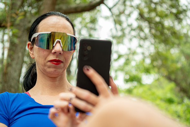 戴着运动太阳镜的女性在公园休息时查看手机信息的特写镜头图片下载