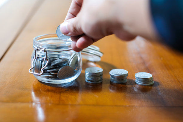 近景:把硬币放在罐子里的手与木桌上的钱堆在一起图片下载