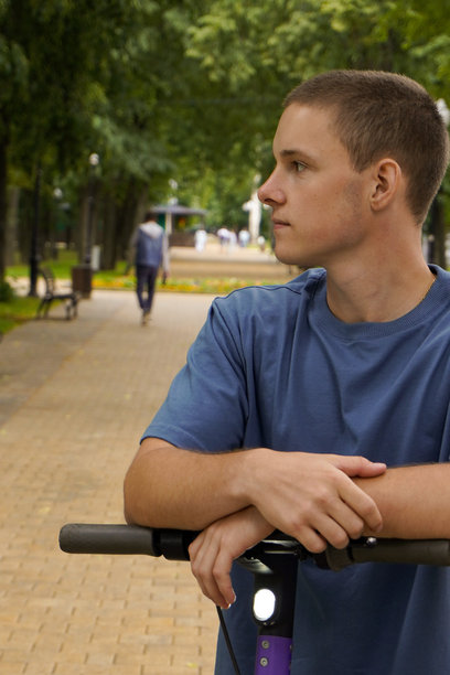 瘦高的男孩骑着电动滑板车在公园里行走，选择性对焦。环保电动交通工具。图片下载