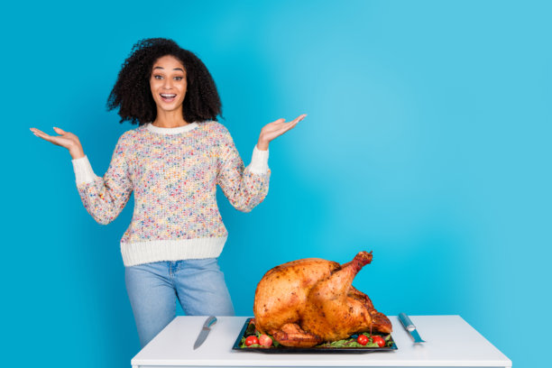吸引人的年轻女性在蓝色背景下兴奋地庆祝感恩节晚餐，手中拿着火鸡的照片肖像图片下载