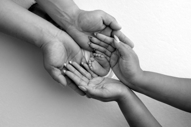 父母的手掌。一位父亲和母亲抱着包裹在毛毯中的新生儿的脚。父母手中握着新生儿的脚。黑白照片，展示脚、脚跟和脚趾。图片下载