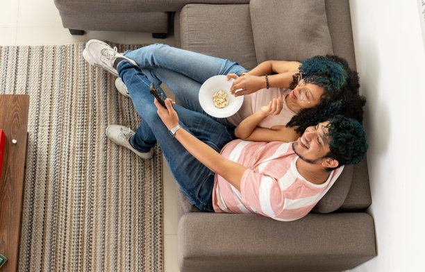 一对相爱的西班牙裔情侣在客厅里拥抱着吃爆米花，一对浪漫的拉丁情侣在沙发上享受看电视的时光和小吃，俯视的视角。图片下载