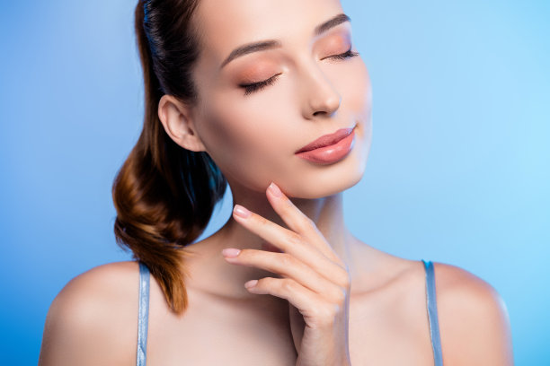 特写剪裁照片，迷人美丽的模特女孩闭着眼睛，轻触面部肌肤，背景为蓝色。图片下载