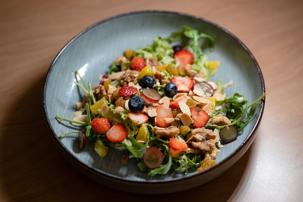 混合水果沙拉配各种坚果，摆放在木桌上的盘子里。健康饮食理念。图片下载