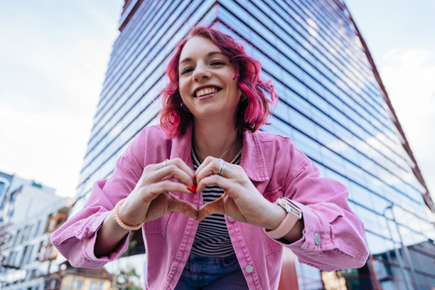 户外一位头发色彩鲜艳的女性用手指做出心形。图片下载