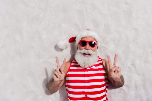 圣诞老人躺在沙滩上，面带微笑，比出V字手势（高角度照片）图片下载