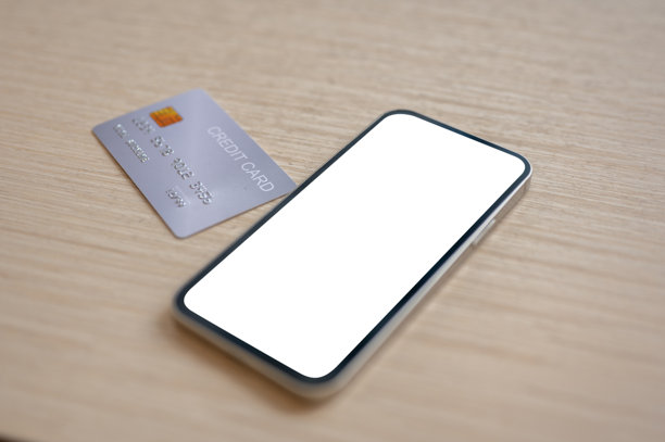 一张信用卡和一部白色屏幕模型的智能手机特写，放置在室内的木桌上。图片下载