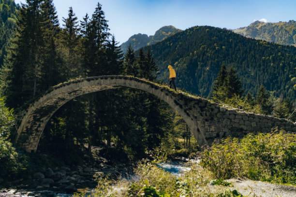 猫桥。卡姆利赫姆辛的古老历史石桥横跨小溪。照片中一名穿着黄色连帽衫的男子正在桥上行走。图片下载