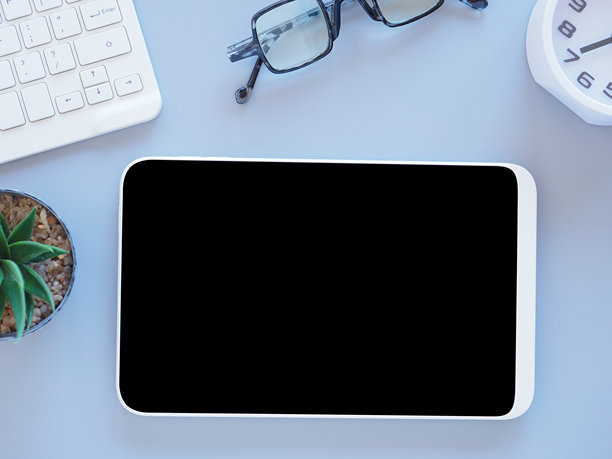 浅紫色背景上的平铺黑色屏幕数字平板电脑模型，旁边有时钟、键盘、眼镜和植物。图片下载