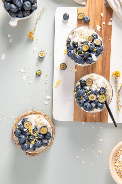 三碗健康的蓝莓柠檬过夜燕麦，上面撒有蓝莓、柠檬皮和椰子屑，放在浅蓝色的木桌上。俯视图。图片下载