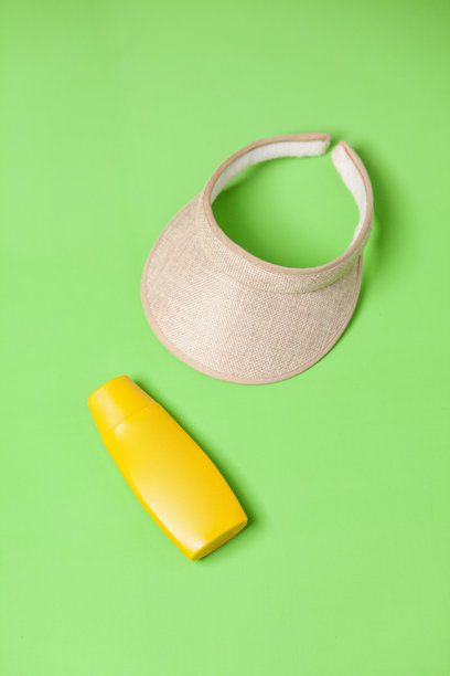 绿色背景上的黄色防晒霜瓶和遮阳帽。图片下载