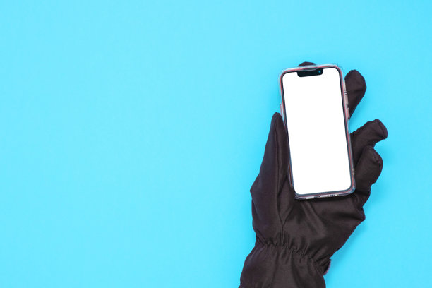 手戴黑色手套的手握着一部蓝色背景下屏幕空白的智能手机图片下载