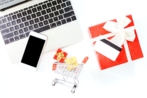 白色背景上方的笔记本电脑、迷你购物车和带信用卡的礼品盒的俯视图图片下载