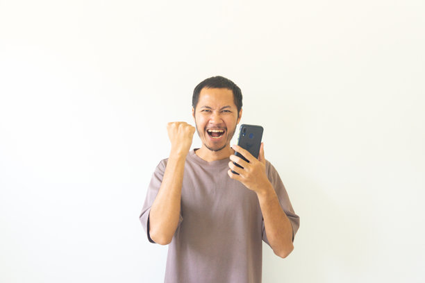 穿着紫色T恤，快乐微笑地拿着智能手机的亚洲年轻男人，积极的反应图片下载