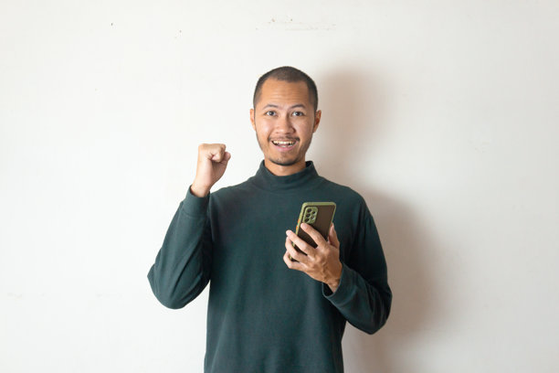 年轻男子穿着冬季服装，在白色背景下庆祝并手持智能手机图片下载