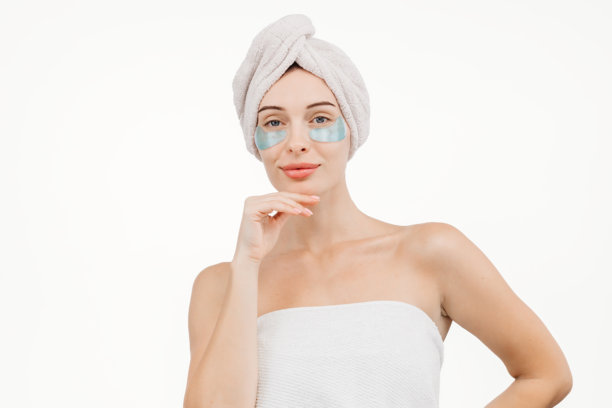 年轻女性的特写，使用眼部贴片针对皱纹和黑眼圈。背景为白色，这张图片强调护肤和对抗疲劳迹象。图片下载