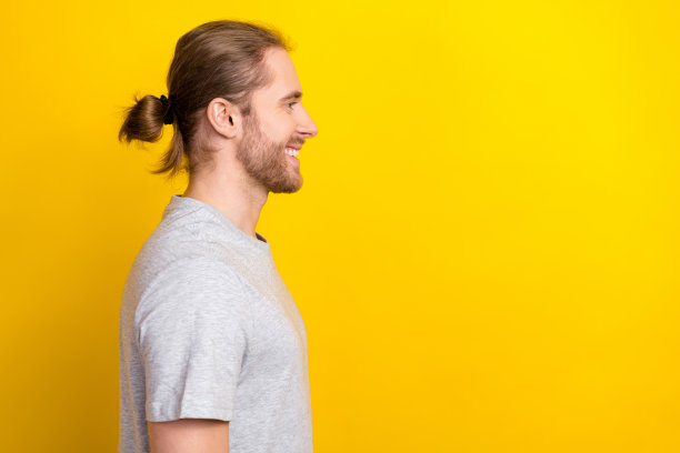 乐观友好的男人侧面照片，穿着灰色T恤，面向空旷的理发店广告，背景为黄色。图片下载