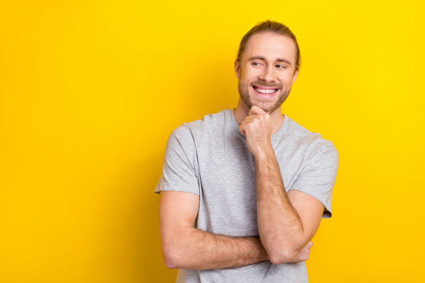 穿着时尚的快乐男人，手臂触碰脸庞，神情有趣，展示新闻，背景为空旷的黄色。图片下载