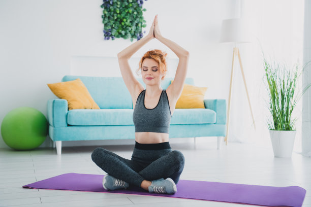 全身照片，年轻运动女性坐在家中健身房的瑜伽垫上练习健身。图片下载