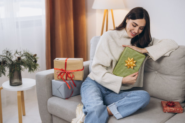 美丽快乐的女人在家沙发上拆开新年或圣诞礼物图片下载