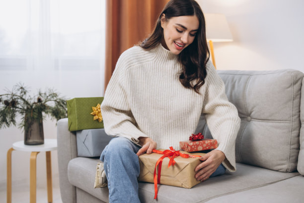 美丽快乐的女人在家沙发上拆开新年或圣诞礼物图片下载