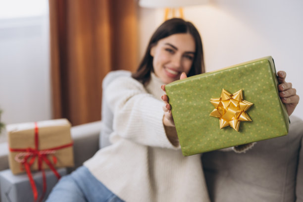 美丽快乐的女人在沙发上拆开新年或圣诞礼物图片下载