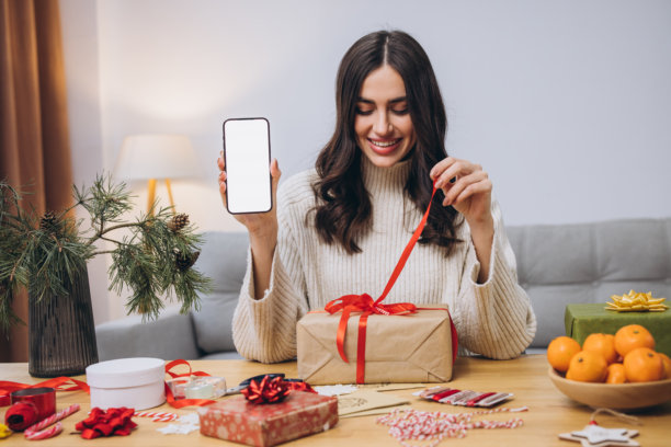 女人在包裹新年或圣诞礼物，同时拿着智能手机。图片下载