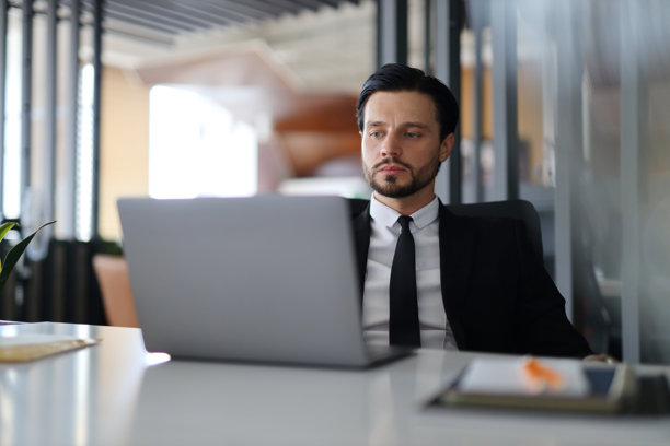 男人身穿西装坐在办公桌前，打开笔记本电脑，专注于工作，专业而高效图片下载