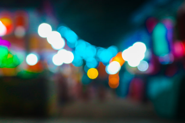 夜市美食摊位的模糊图像，背景为五光十色的灯光和虚化效果。夜间节日城市公园的抽象照片，模糊的人群与灯光交织。图片下载