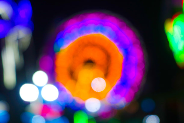 夜间节日中模糊的摩天轮图像，背景为散景。城市公园夜间节日中游戏设施的抽象模糊照片，背景为五光十色的灯光。图片下载