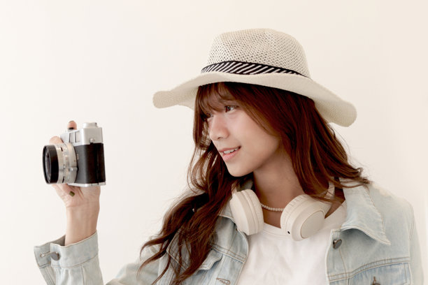 穿着牛仔夹克和夏季帽子的亚洲年轻女性旅行者，手持胶卷相机准备拍摄一张令人印象深刻的照片。背景中是一位年轻女性游客与她的经典老式胶卷相机。旅行女孩带着相机前往她的目的地。图片下载