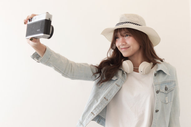 穿着牛仔夹克和夏季帽子的亚洲年轻女性旅行者，手持胶卷相机准备拍摄一张令人印象深刻的照片。背景中是一位年轻女性游客与她的经典老式胶卷相机。旅行女孩带着相机前往她的目的地。图片下载