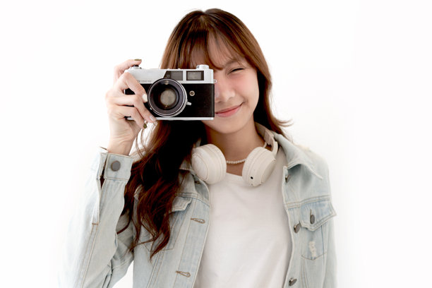 穿着牛仔夹克和夏季帽子的亚洲年轻女性旅行者，手持胶卷相机准备拍摄一张令人印象深刻的照片。背景中是一位女性青少年游客与她的经典老式胶卷相机。旅行女孩带着相机前往她的目的地。图片下载