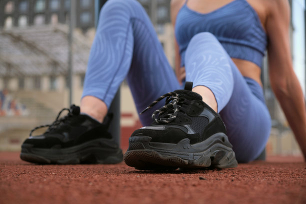 特写镜头展示了一位女性的黑色运动鞋和蓝色运动服，聚焦于运动装备。这张图片突显了高质量运动鞋在有效锻炼中的重要性。图片下载