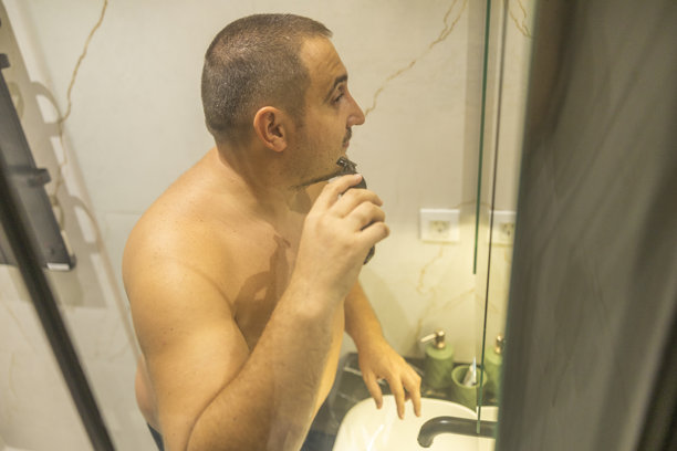 站在浴室里用电动剃须刀刮胡子的超大号男人照片图片下载