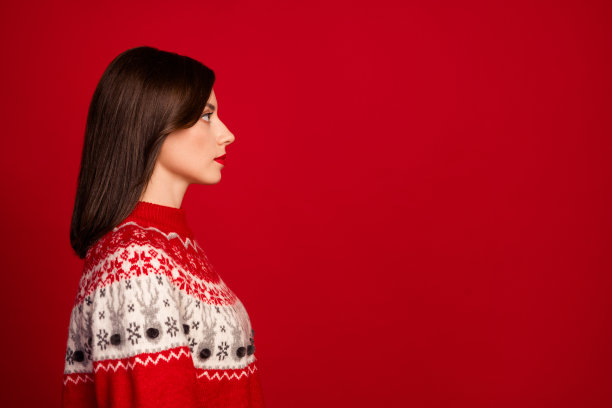 侧面照片，展现了一位可爱、心情愉悦的女性，短发，穿着红色毛衣，面向空旷的空间，背景为红色。图片下载