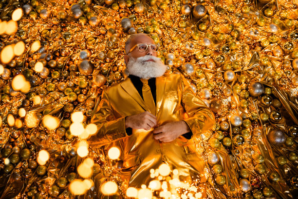 俯视照片，时尚潮流的祖父躺在圣诞球装饰旁，穿着光泽感的节日西装。图片下载