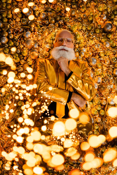 俯视照片中，严肃而酷的祖父躺在圣诞树装饰旁，金色的光芒中思考着魔法与奇迹。图片下载