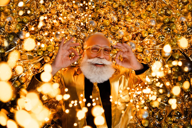 俯视照片中，快乐的祖父躺在装饰有圣诞树球的灯光下，做出“好”的手势。图片下载