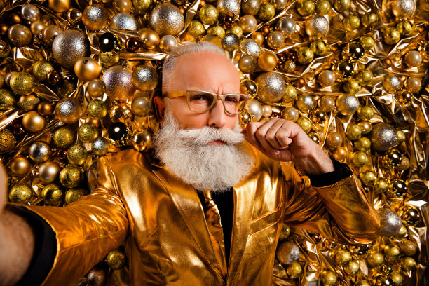 从上方拍摄的照片，严肃而酷的老祖父在圣诞树装饰前摸着胡子自拍。图片下载