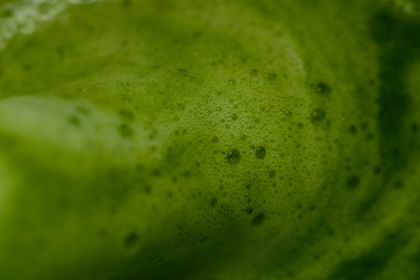 一张特写的绿茶图片，展现出光滑、泡沫丰富的质感。鲜艳的绿色和表面可见的气泡突显了茶的鲜度和品质。茶水的光泽反射也很明显。图片下载
