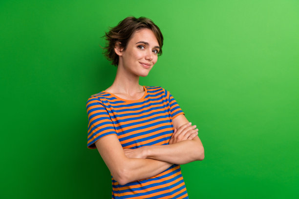 漂亮年轻女孩的照片肖像，双手交叉自信摆姿，穿着时尚条纹服装，背景为绿色。图片下载